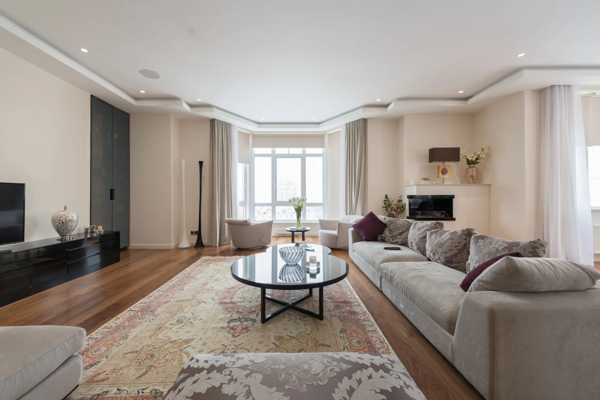Comfortable sofa with cushions placed in front of coffee table and modern TV in spacious elegant living room decorated with ornamental carpet and flowers vases