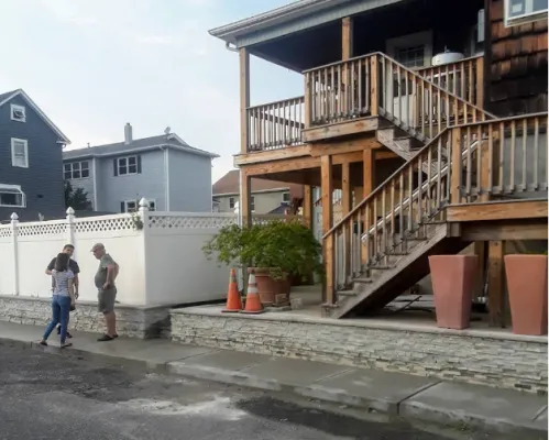 3 people standing outside of a building with multi levels of stairs; large plants in pots on the walkway