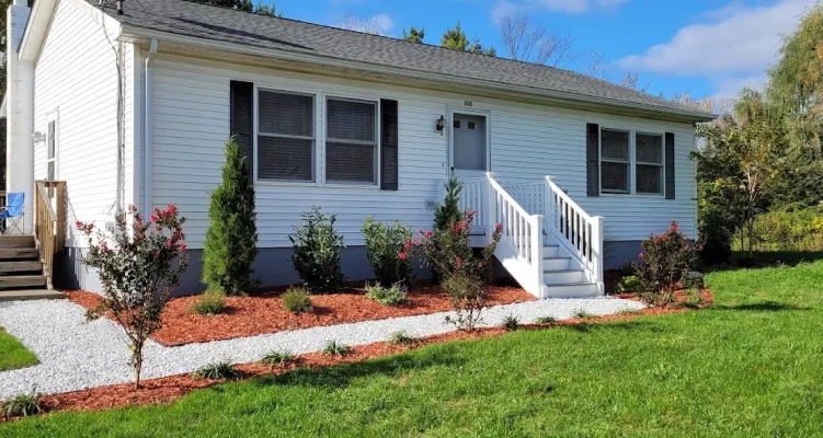 A charming white house with beautiful landscaping, including new trees, rose bushes, and freshly spread mulch