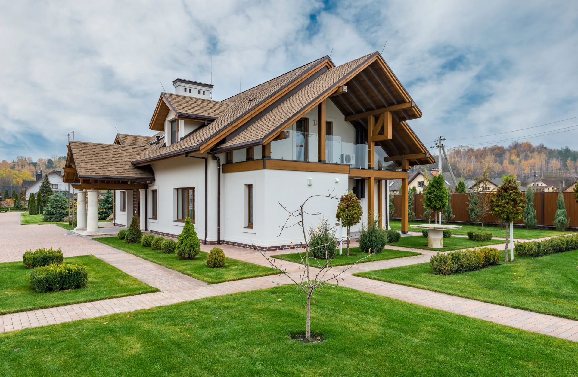 Exterior of modern cottage house with columns and balcony surrounded by green grass and trees
