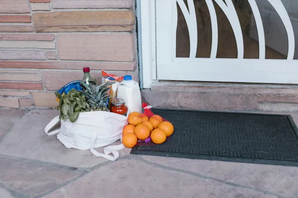Reusable bag with groceries and fruits left at doorstep, highlighting delivery service.