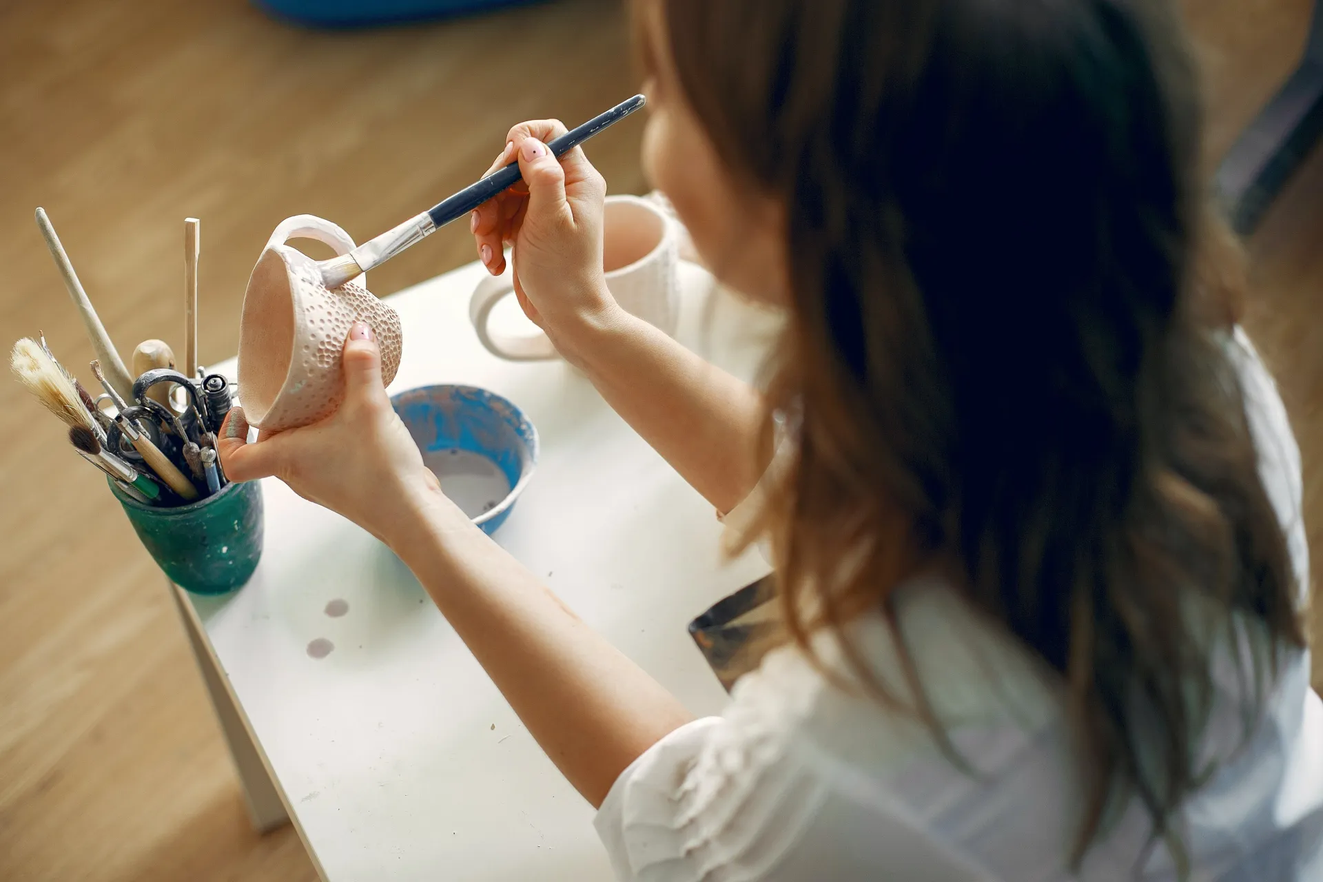 Crop female artisan painting clay pieces on table