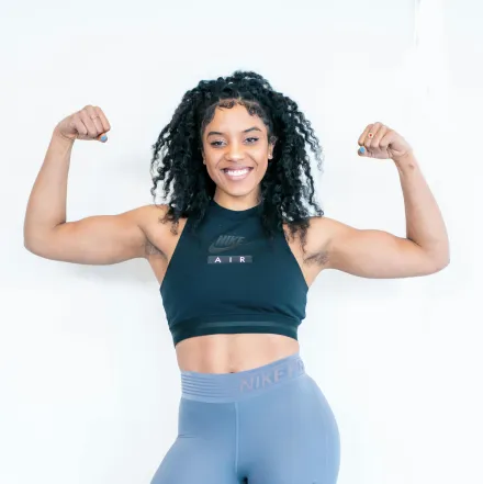Strong woman posing indoors, showcasing fitness and strength with a confident smile.