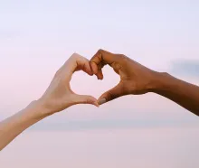 A powerful image of unity and diversity with two hands forming a heart against a serene pastel sky.