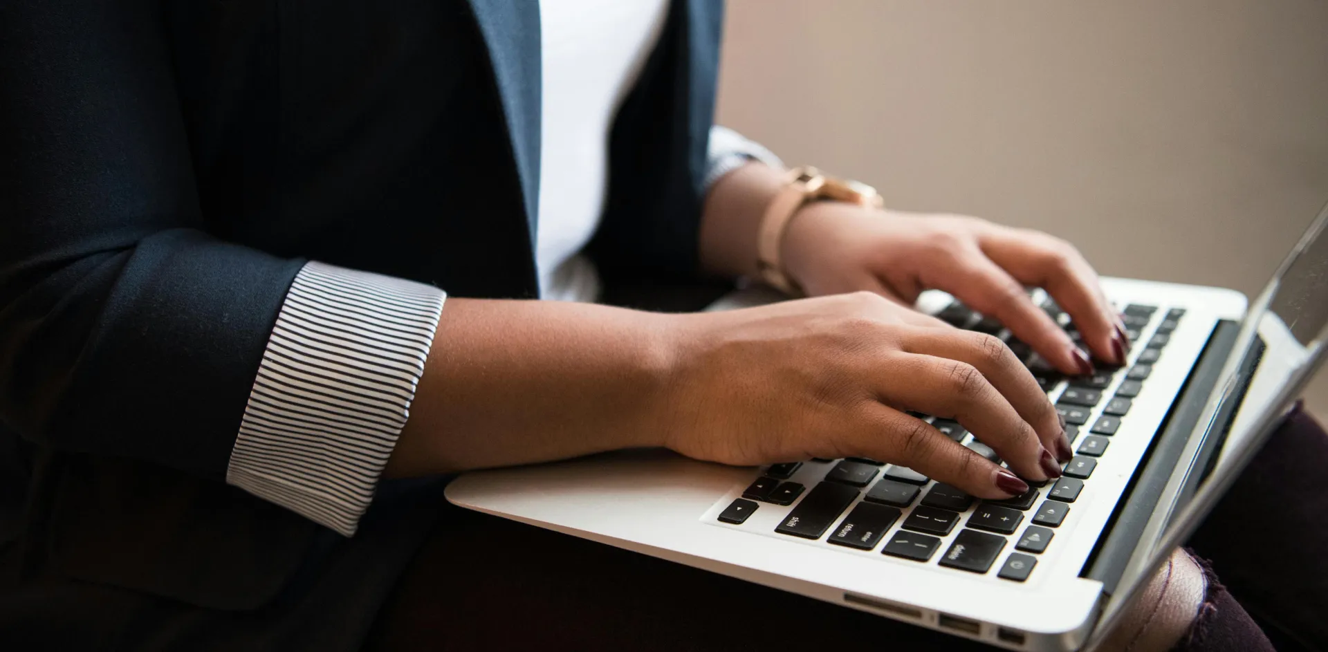 Woman in a blazer typing on a laptop in a well-lit room, focused on remote work.