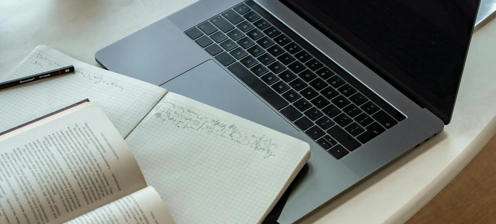 A cozy indoor workspace featuring a laptop, open book, notepad, and coffee, perfect for studying or remote work.