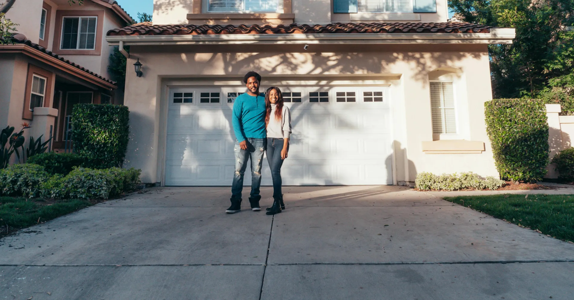 Smiling couple standing outside their newly purchased house on a sunny day.