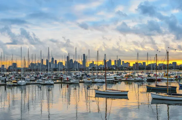 A stunning view of a marina with numerous sailboats and a vibrant city skyline at sunset.