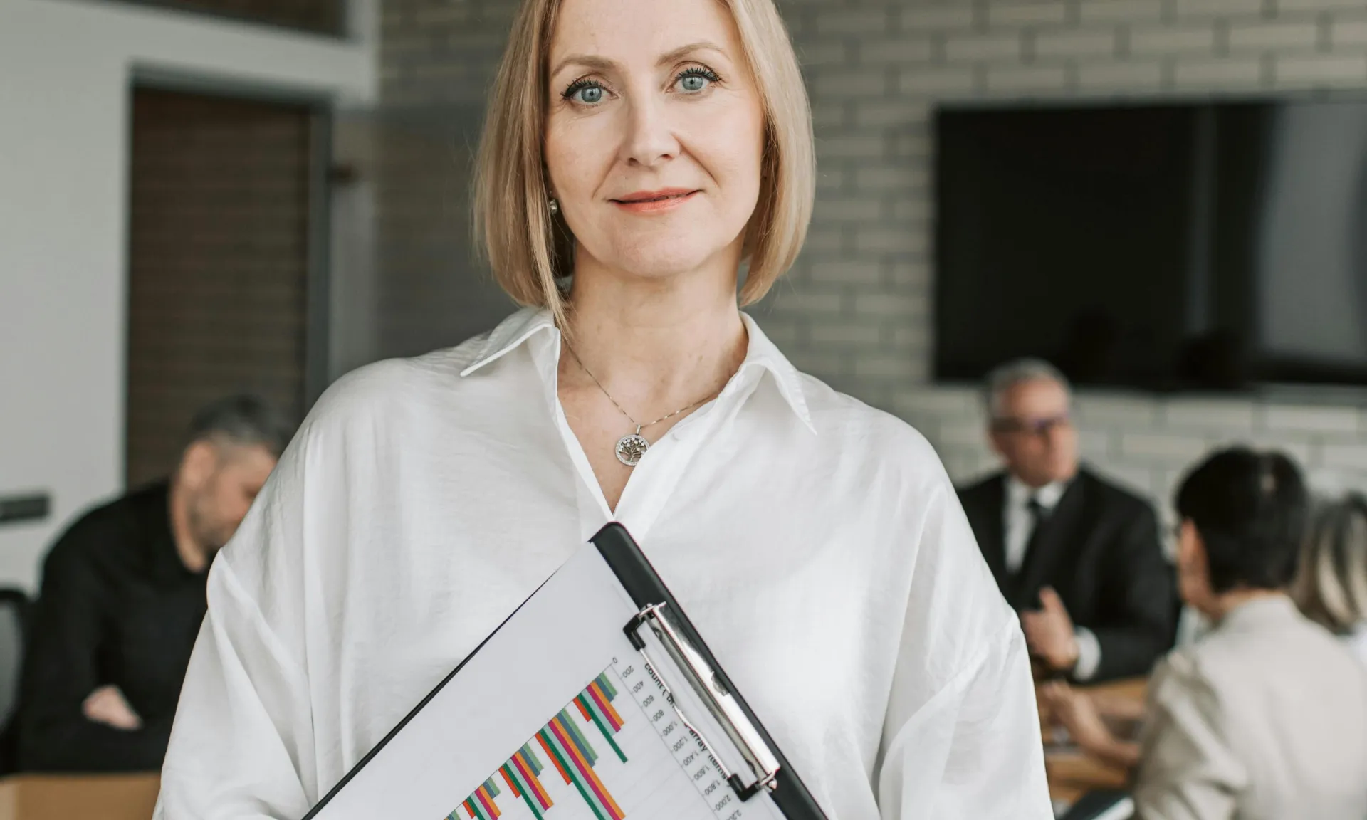 Professional woman holding clipboard in corporate office setting during a business meeting.