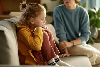 Sad baby sitting alone on a couch, looking down with a solemn expression