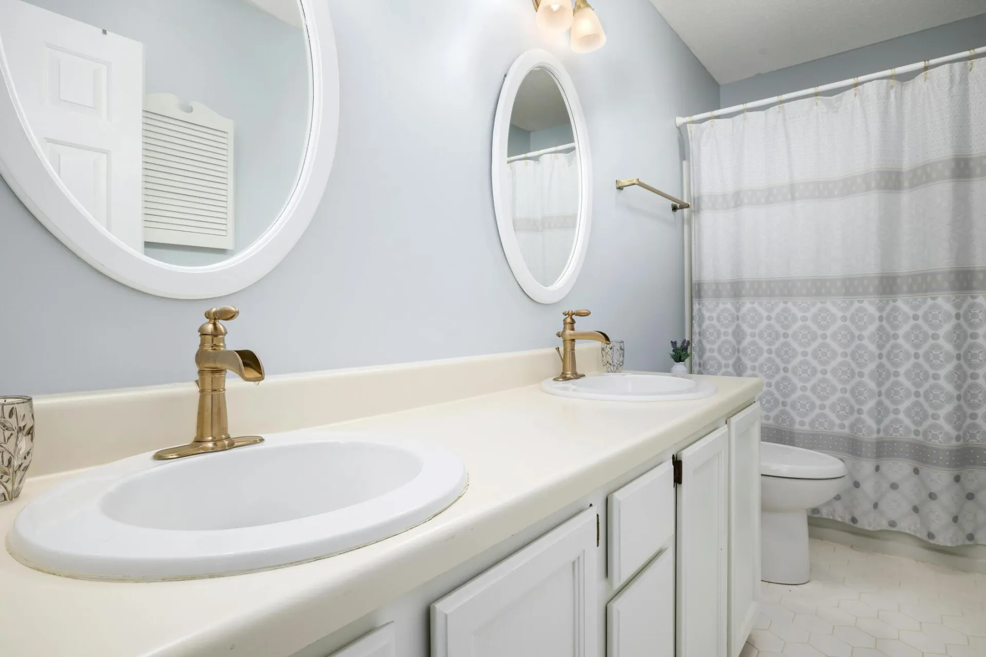 A modern bathroom featuring dual sinks with gold faucets, round mirrors, and a shower curtain.