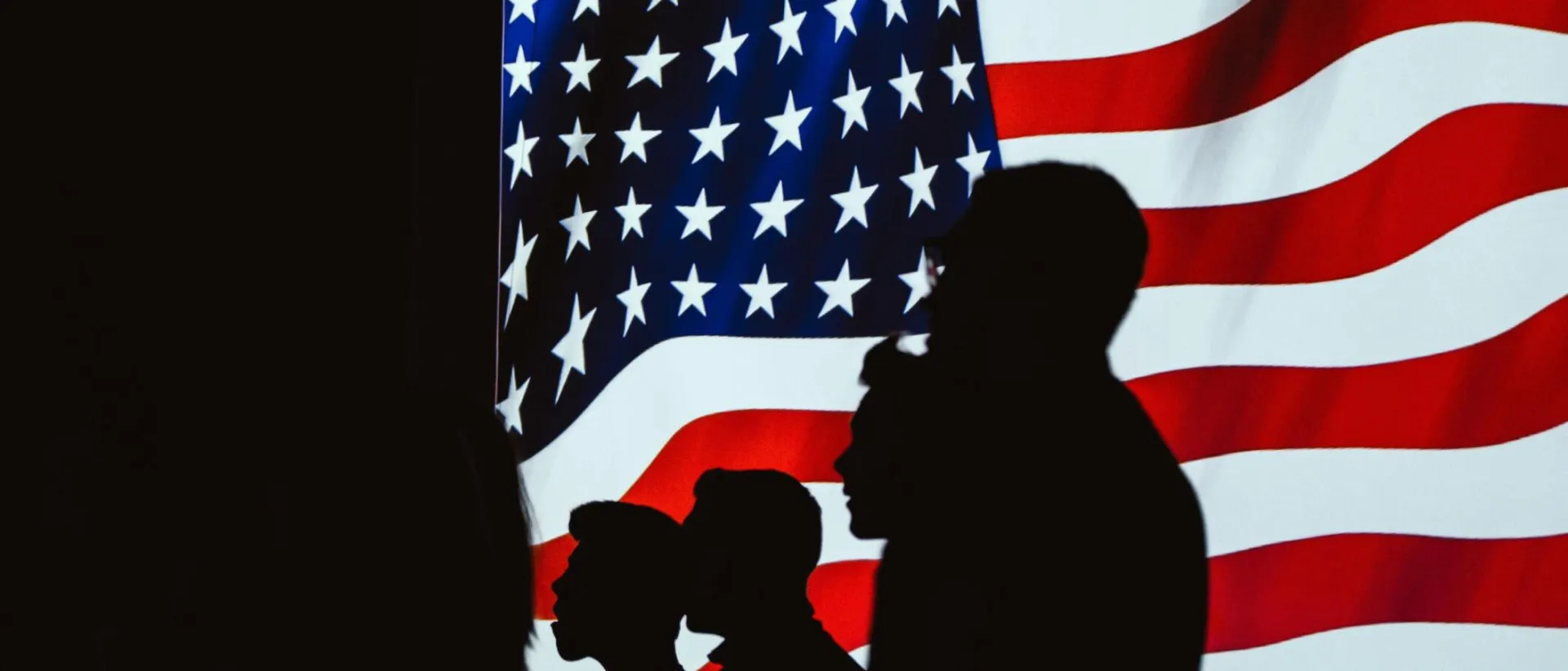 Silhouetted figures in front of a bright, wavy American flag create a patriotic scene.
