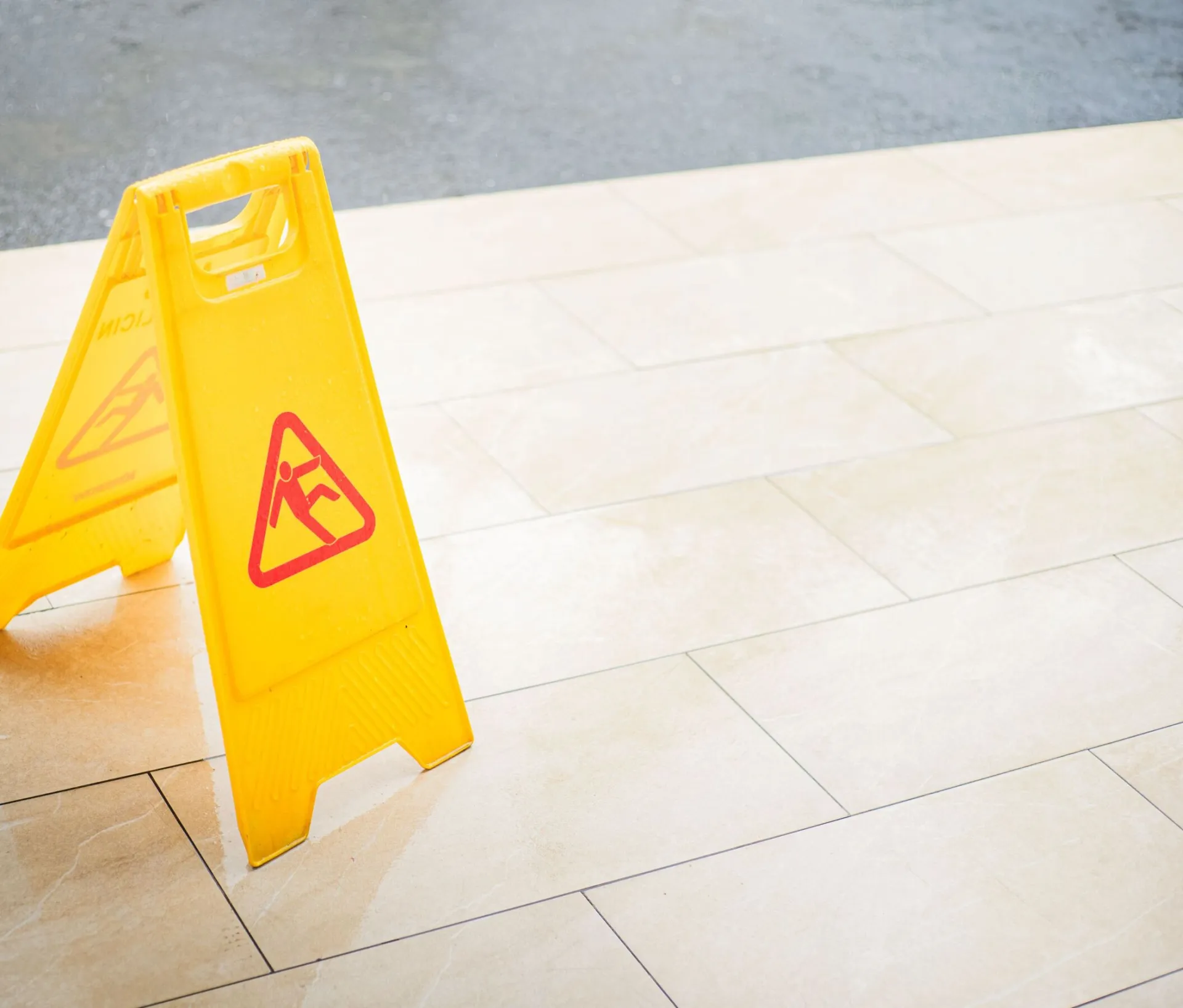 A bright yellow caution sign placed on a tile floor indicating a wet area for safety.