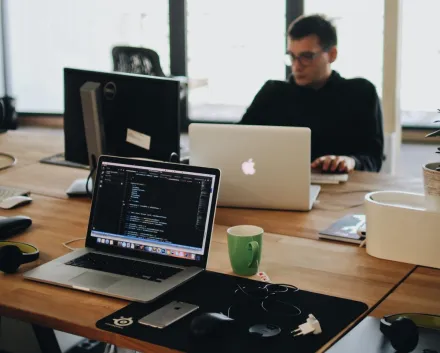 Man in Black Shirt Sits Behind Desk With Computers