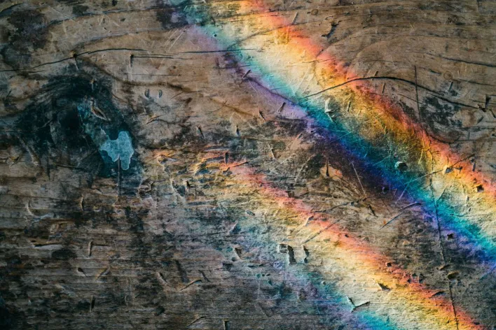 Vibrant rainbow reflections create a fascinating pattern on an aged wooden surface.