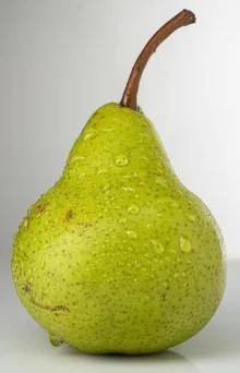 Vibrant green pear with water droplets on a neutral background, highlighting freshness.
