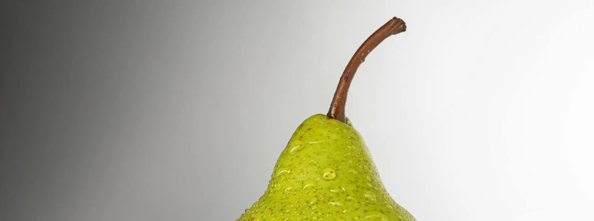 Vibrant green pear with water droplets on a neutral background, highlighting freshness.