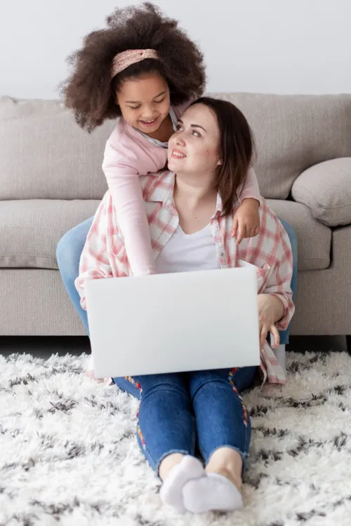 A relaxed pregnant woman working remotely on a laptop from home on a cozy green couch.