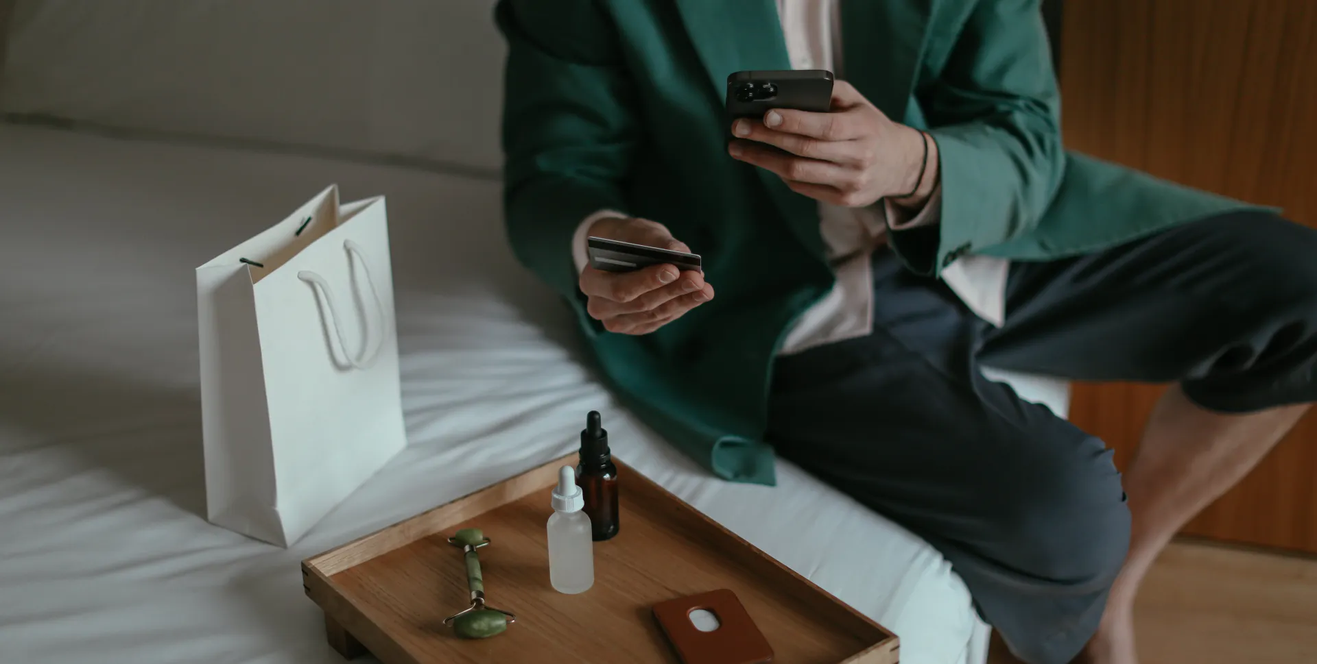 Anonymous man using smartphone while placing order with credit card sitting near cosmetic products