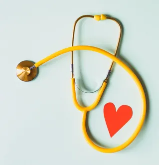 Medical stethoscope with red paper heart on white surface