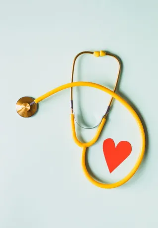 Medical stethoscope with red paper heart on white surface