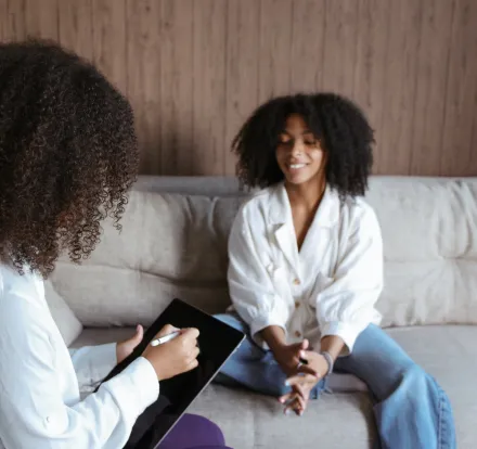 A Woman Sitting on the Couch Talking to the Woman Holding a Tablet