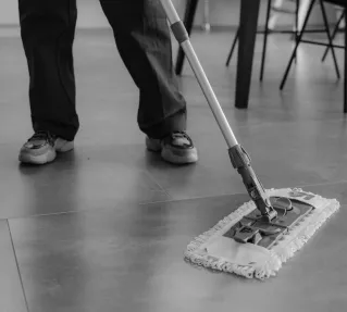 Monochrome image of a person mopping a tiled floor in an indoor setting.