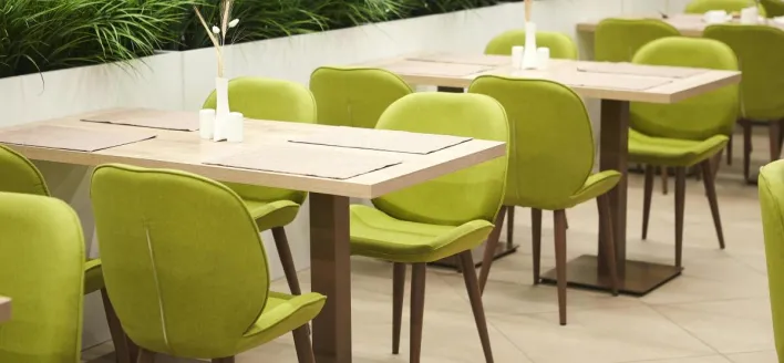 Contemporary dining area with green chairs and wooden tables indoors.
