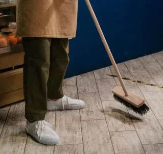 A barista in an apron sweeps the café floor, maintaining cleanliness in a cozy indoor setting.