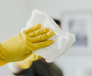 Anonymous male wearing yellow latex gloves and dark t shirt wiping mirror in bathroom with paper napkin