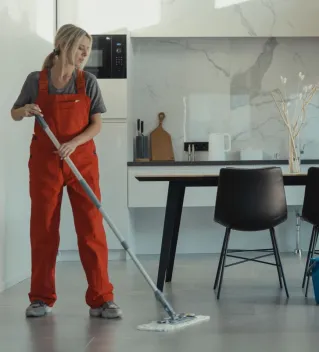 Group of cleaners in red uniforms mopping and wiping glass in a modern dining room.