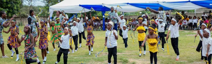 Children in traditional attire performing a lively dance at an outdoor event in Winneba, Ghana.