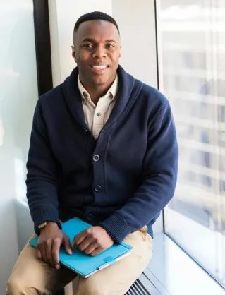 A professional black man smiling while seated by a window, embodying modern business vibes.