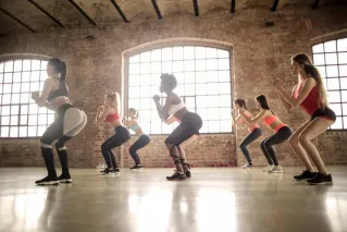Women participating in a group fitness class performing squats in an industrial-style studio.