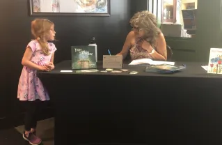 Gail signing a book and a little girl looking on