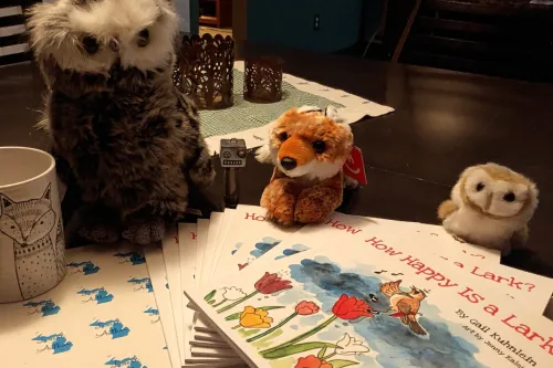 How Happy Is a Lark? stack of books, stuffed owls and fox next to books, a fox mug and some Local Author Michigan stick