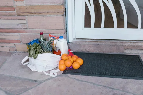 Reusable bag with groceries and fruits left at doorstep, highlighting delivery service.