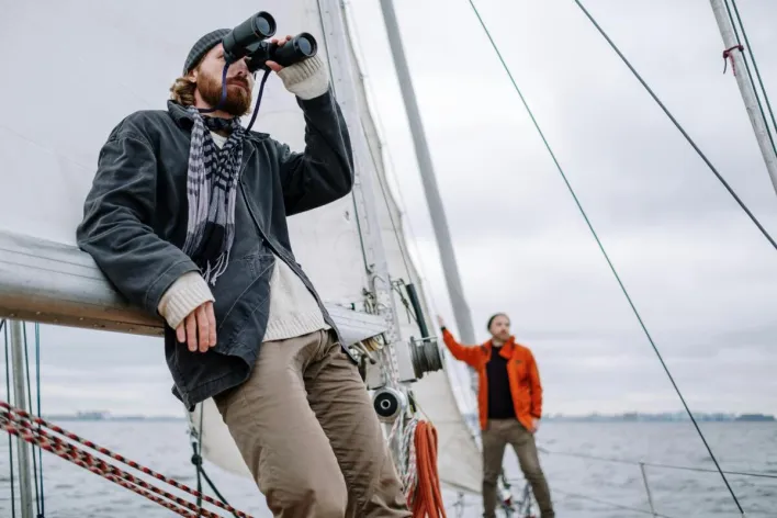 Sailor Looking Around Through Binoculars from the Deck of a Sailboat