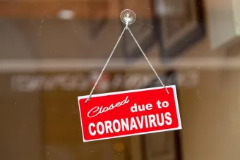 Red sign hanging at the glass door of a shop saying "Closed due to coronavirus". GETTY