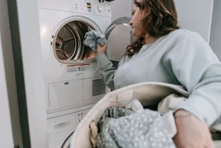 Side view of serious female in casual wear putting laundry into modern washing machine while doing housework in light room at home