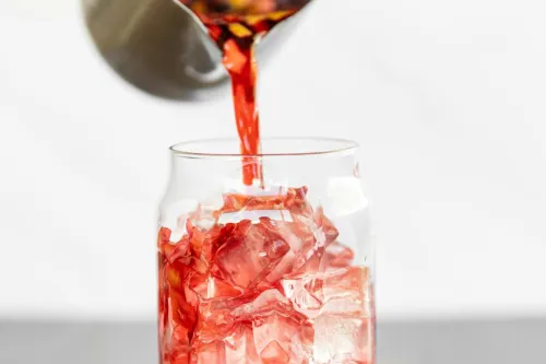 Refreshing hibiscus tea being poured over ice cubes in a clear glass, capturing a vibrant burst of color.