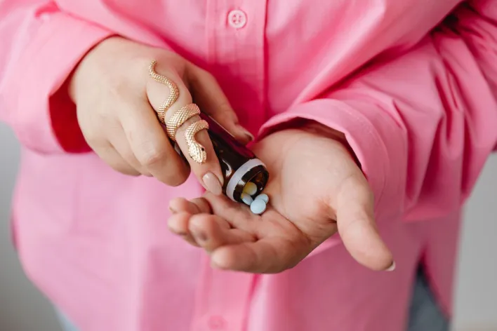 Close-up of hands pouring medicine pills from a bottle, wearing a stylish gold snake ring.