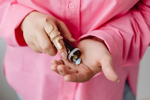Close-up of hands pouring medicine pills from a bottle, wearing a stylish gold snake ring.
