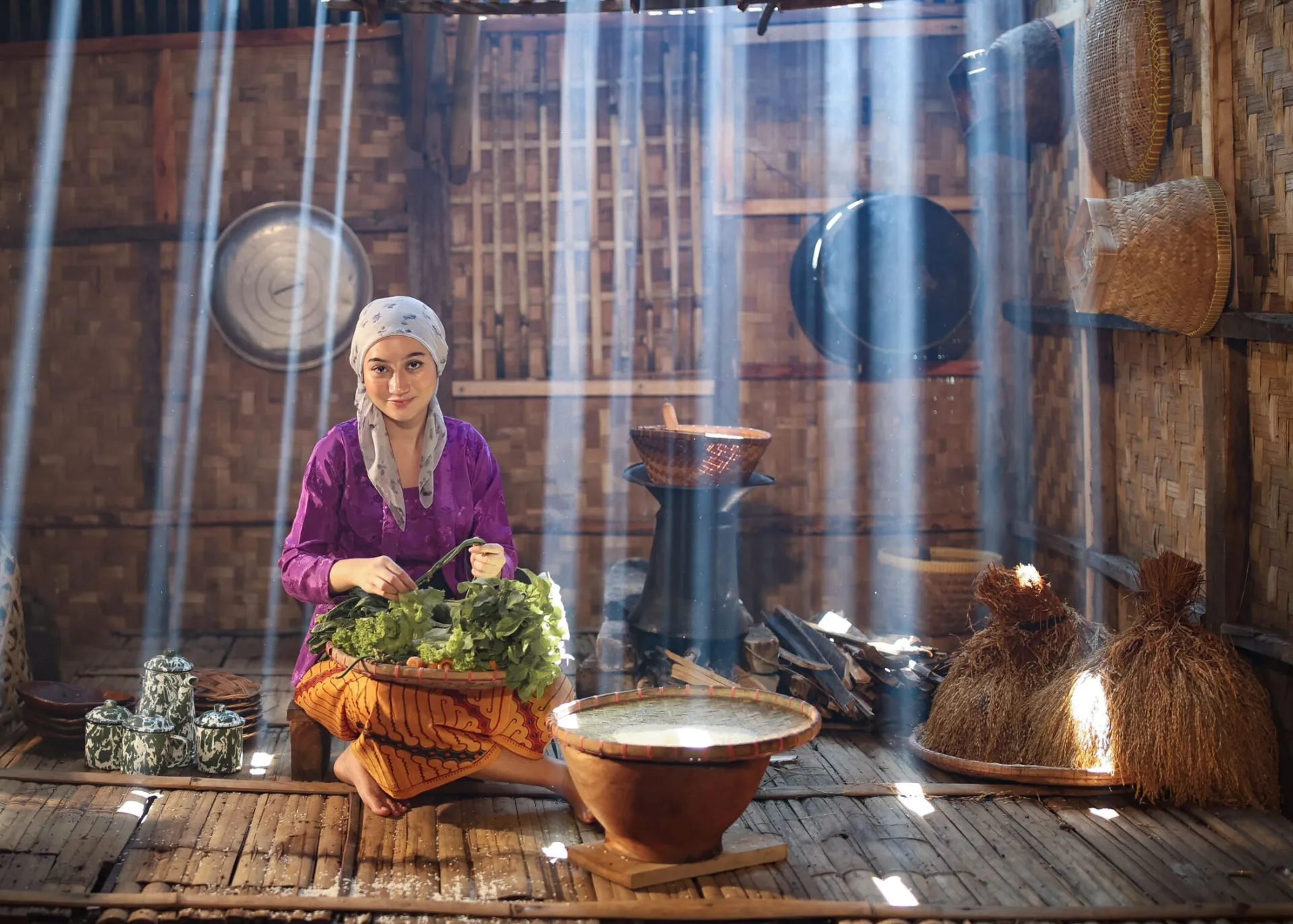 Woman in bamboo hut preparing fresh vegetables under beams of sunlight. Traditional Asian cooking scene