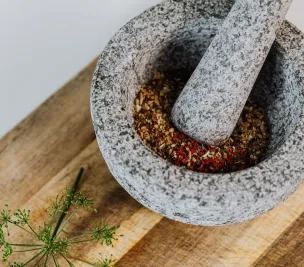 Close-up image of a stone mortar and pestle with a mix of spices on a wooden surface.
