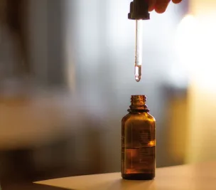 Close-up shot of a serum dropper above an amber bottle, with a soft blurred background and glowing light.