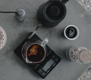 Aerial view of coffee brewing setup with pour-over, grinder, and scale on a textured surface.