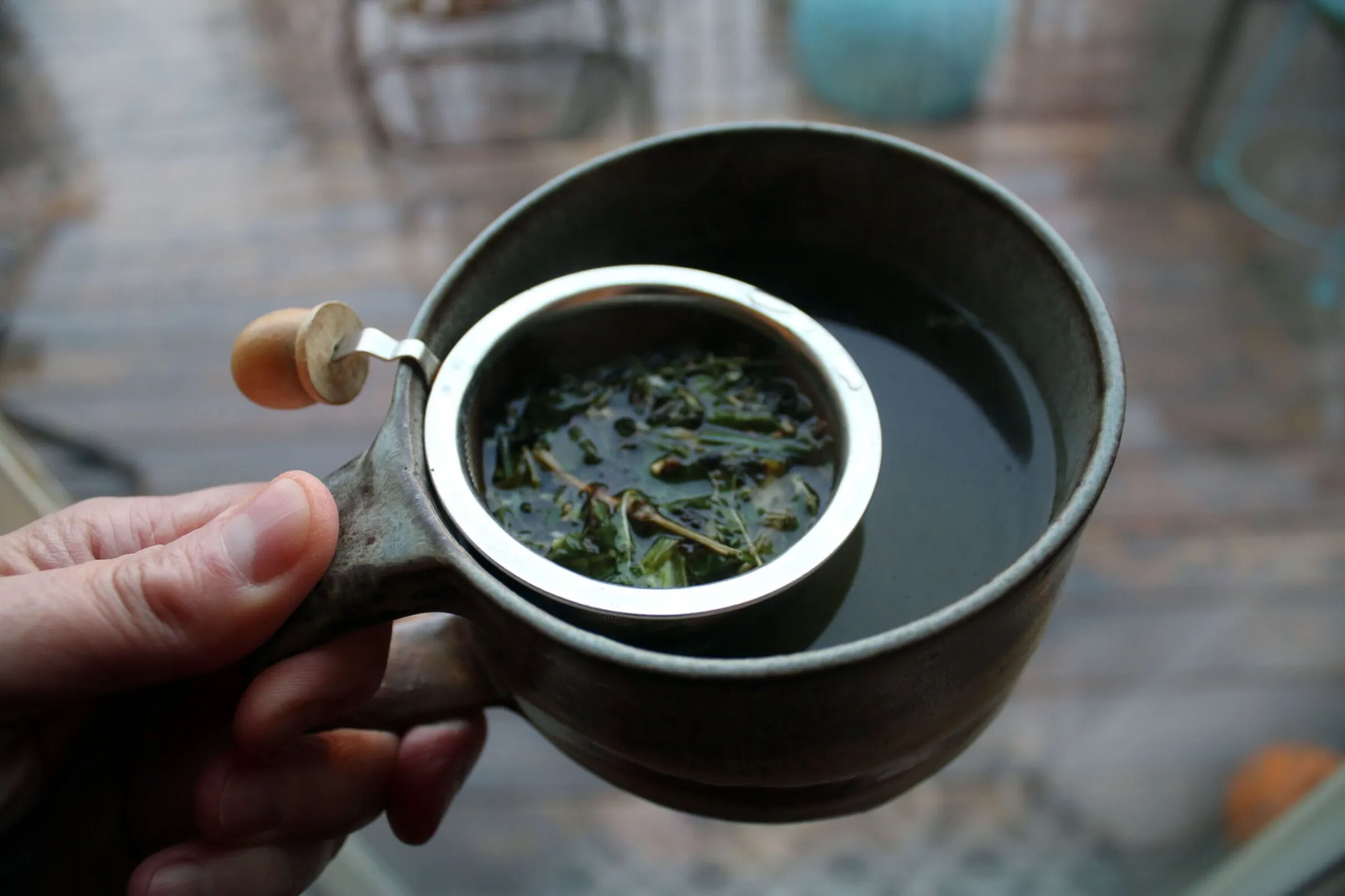 A hand holding a cup of green tea with a strainer, showcasing fresh tea leaves.