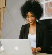 Woman in Black Blazer Sitting by the Table While Using Macbook