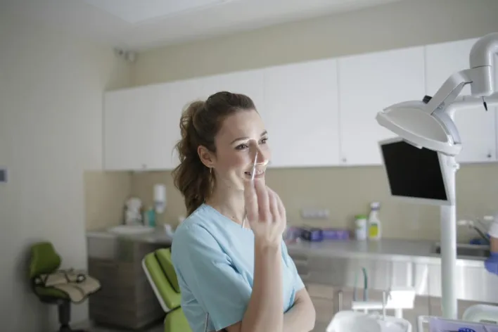 Smiling female dentist in uniform standing with dental tweezers